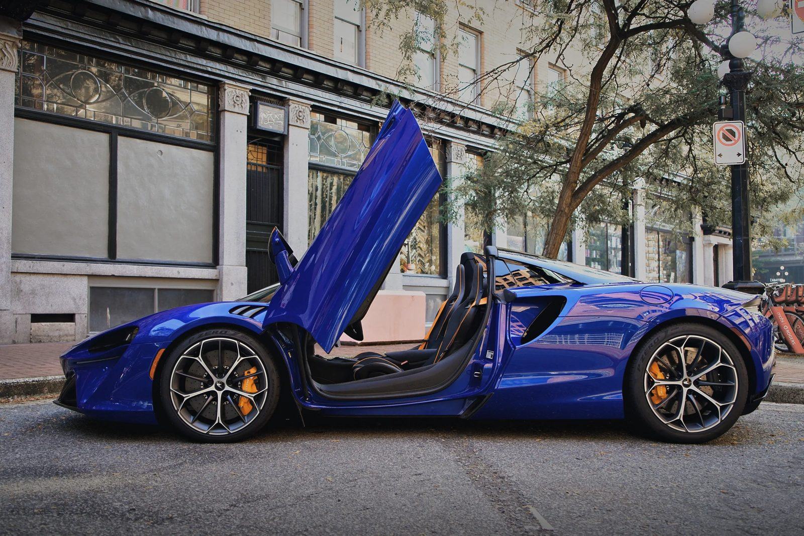 A blue McLaren Artura Spider parked on a Gastown street, door raised.