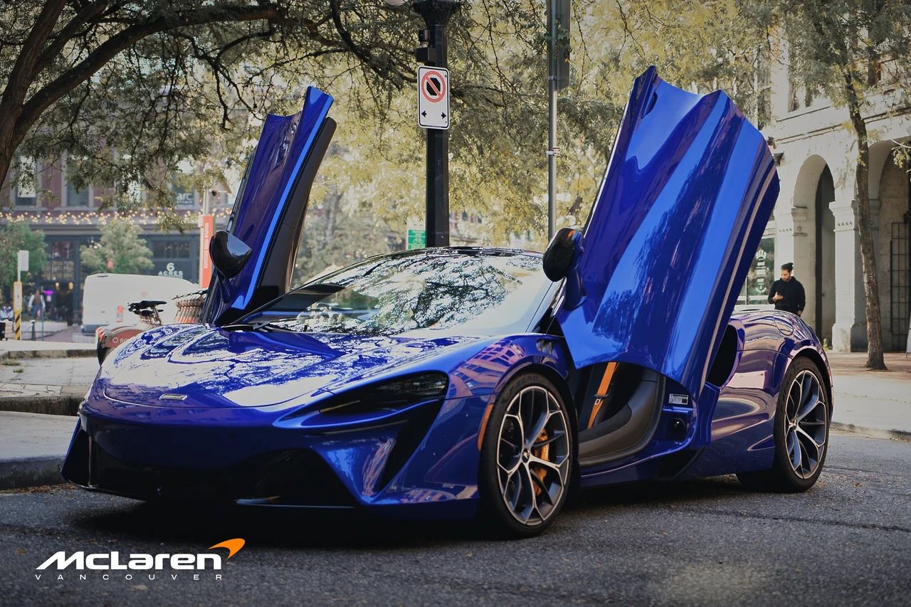 The blue Artura Spider from the front, both doors raised, on a Gastown street.