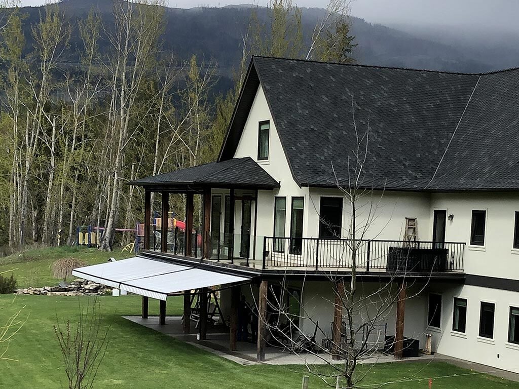 A white farmhouse in the trees with a retractable awning over the lower deck.