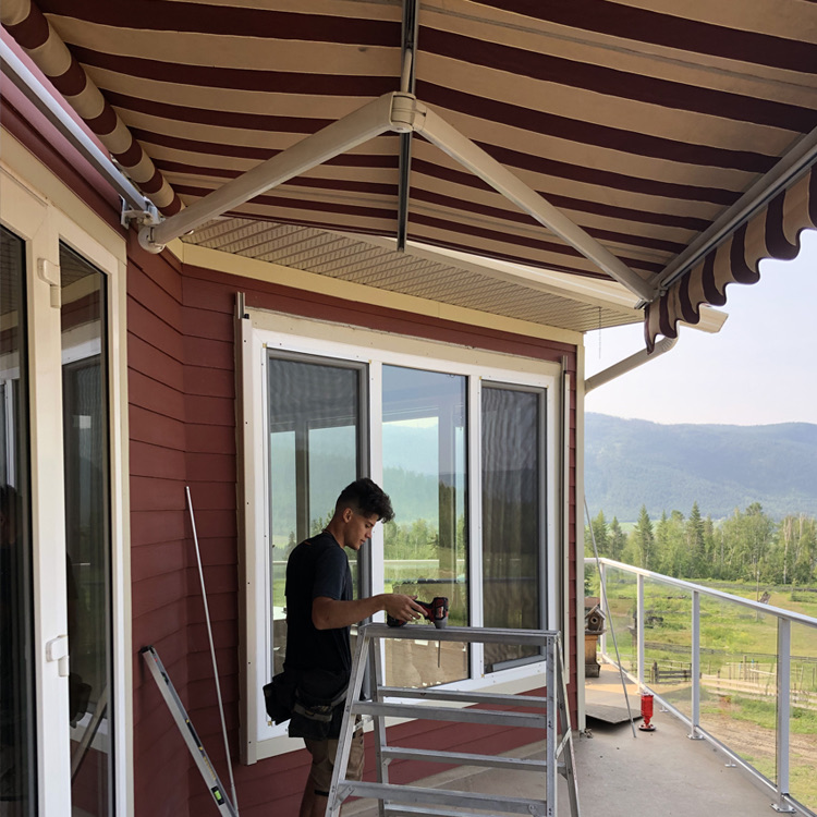 An installer on a ladder fitting an awning to a red house.