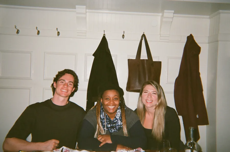 Three members at a table under a row of coat hooks, photographed on film